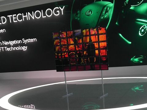 A small grid of iPads on two stands in the middle of a lit circular stage, in front of a Kia display.