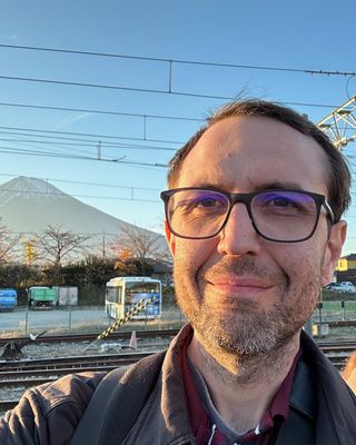 Jeffrey, outside a small train station, with Mount Fuji behind him in evening light.