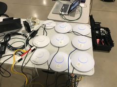 Eight white ceiling-mount access points laid out on a table, each labeled with a letter, cabled to a switch.