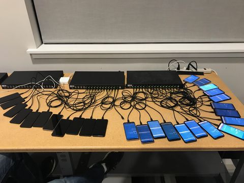 Two rack-mount USB charging hubs on a table with about thirty phones cabled to them.